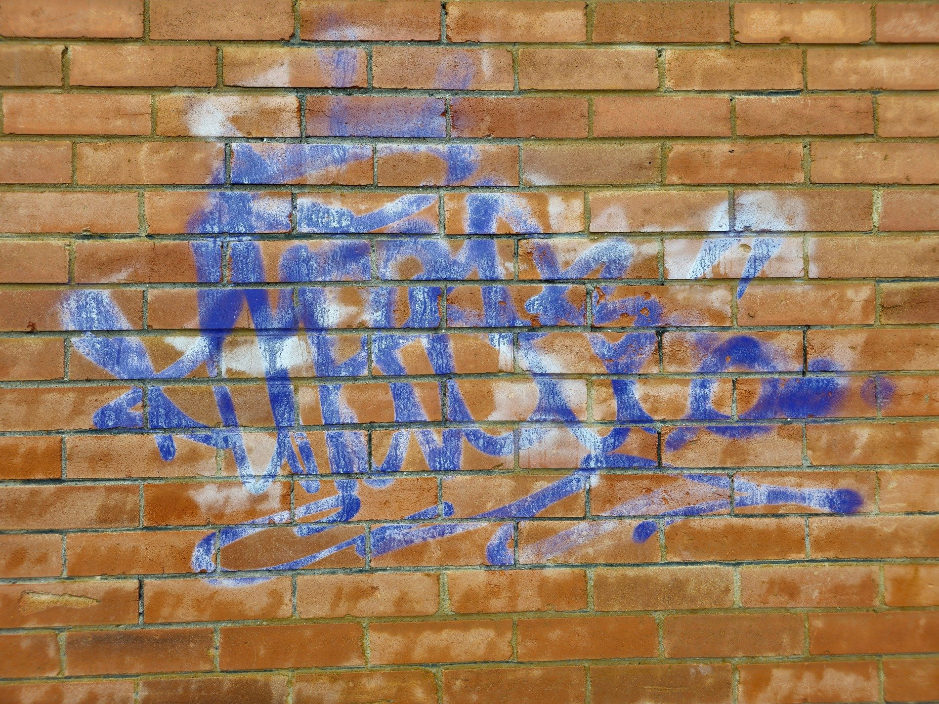 Red clay bricks aligned, blue spray drifts across the wall, urban marks remain