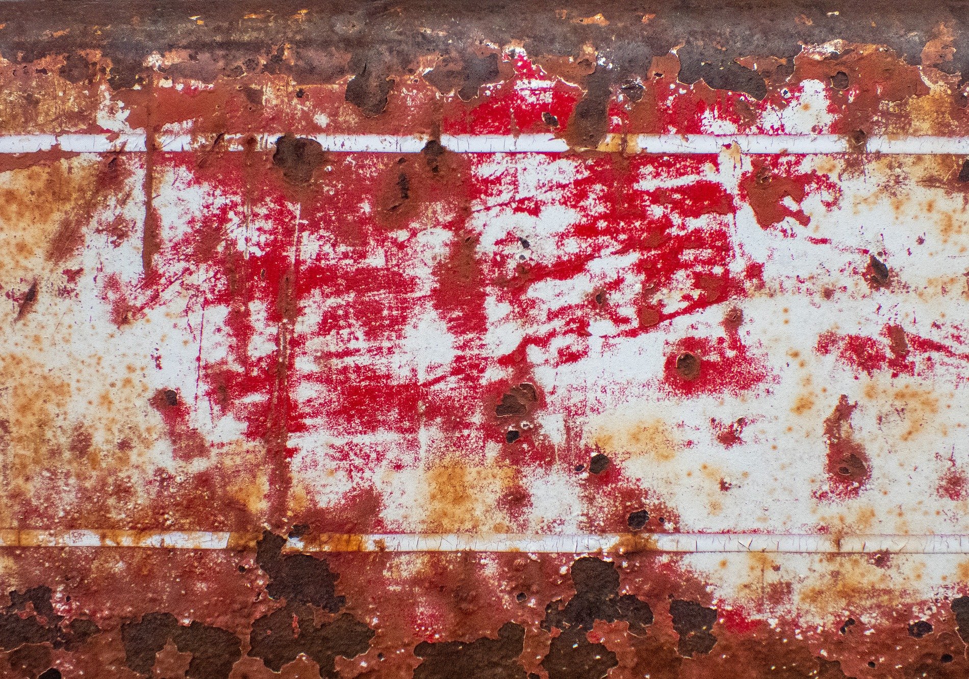 Red paint chips away, oxidation scars the steel, white lines drift in rust