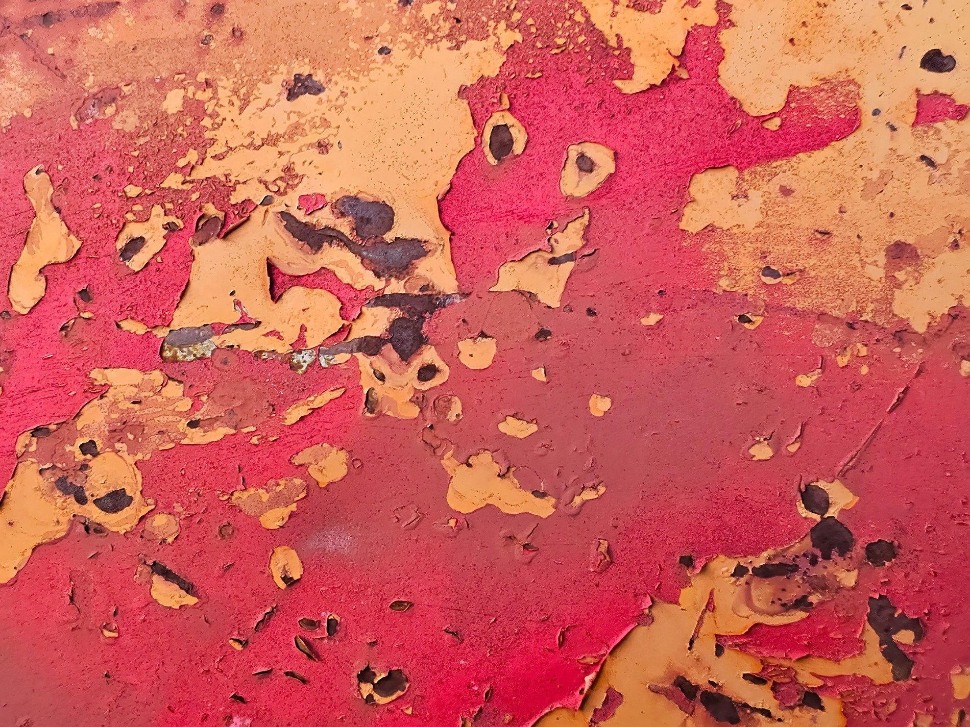 Red paint curls away, yellow cracks on metal skin, rust blooms underneath