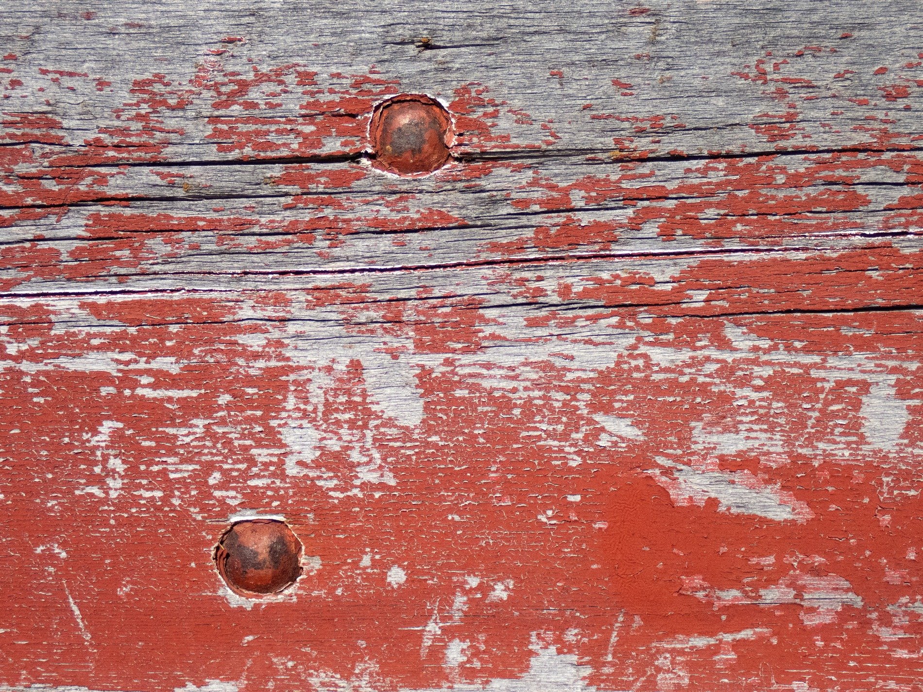 Red paint flakes away, rusty iron bites the wood, grain shows through the age