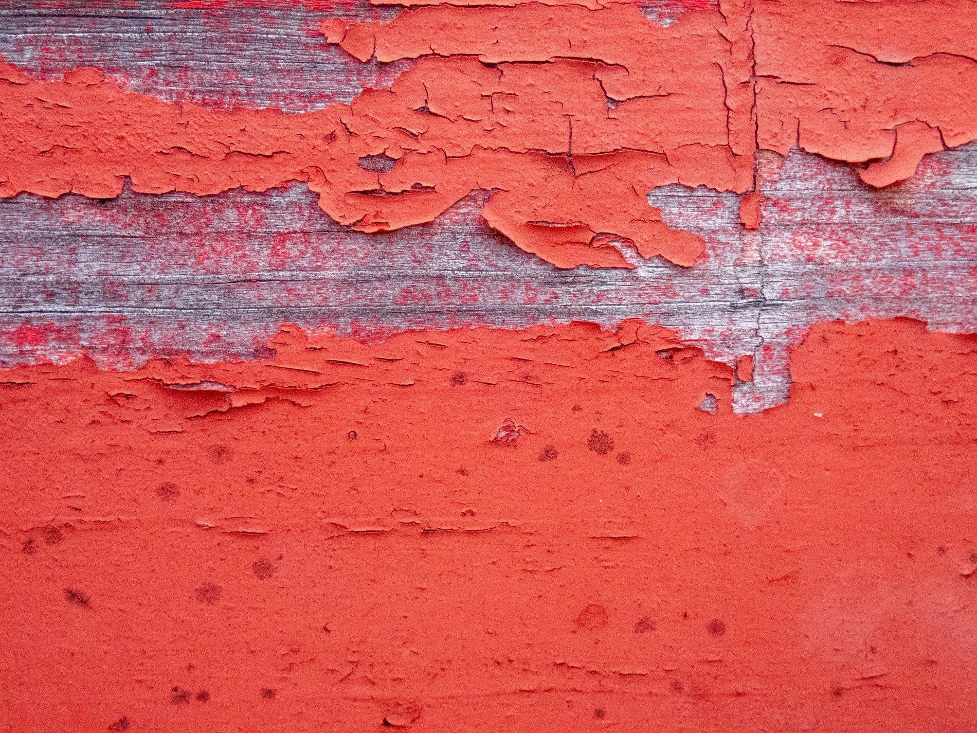 Red paint peels away, silvered wood grain shows below, beauty in decay