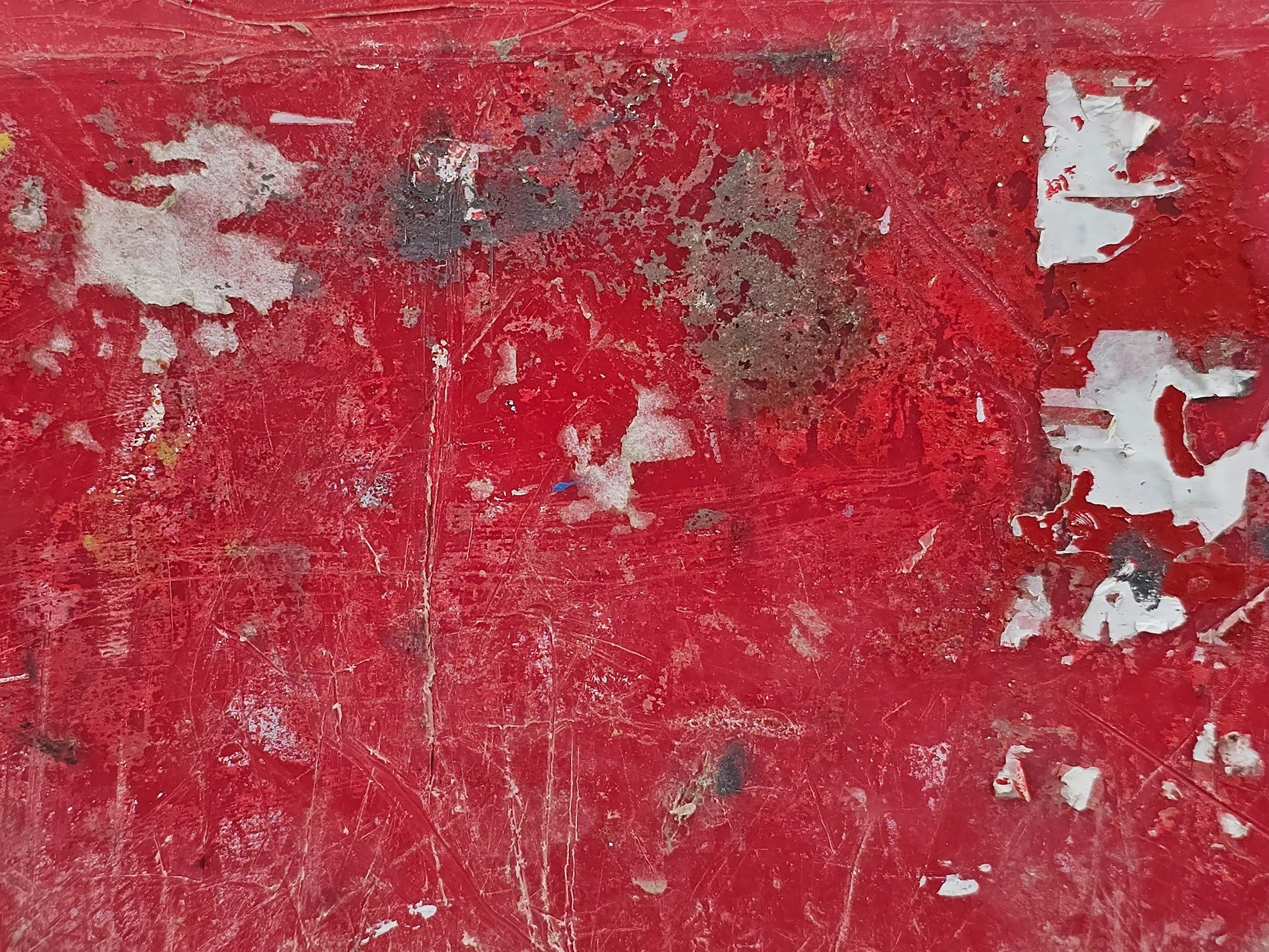 Red paint peels away, white fragments cling to the base, scratches mark the skin