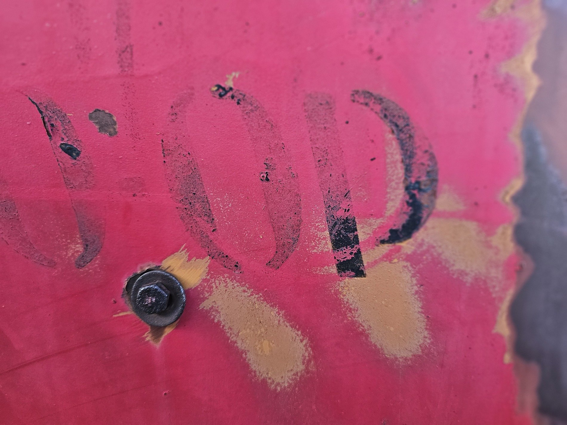 Red paint starts to peel, black letters fade into rust, steel bolt holds its place