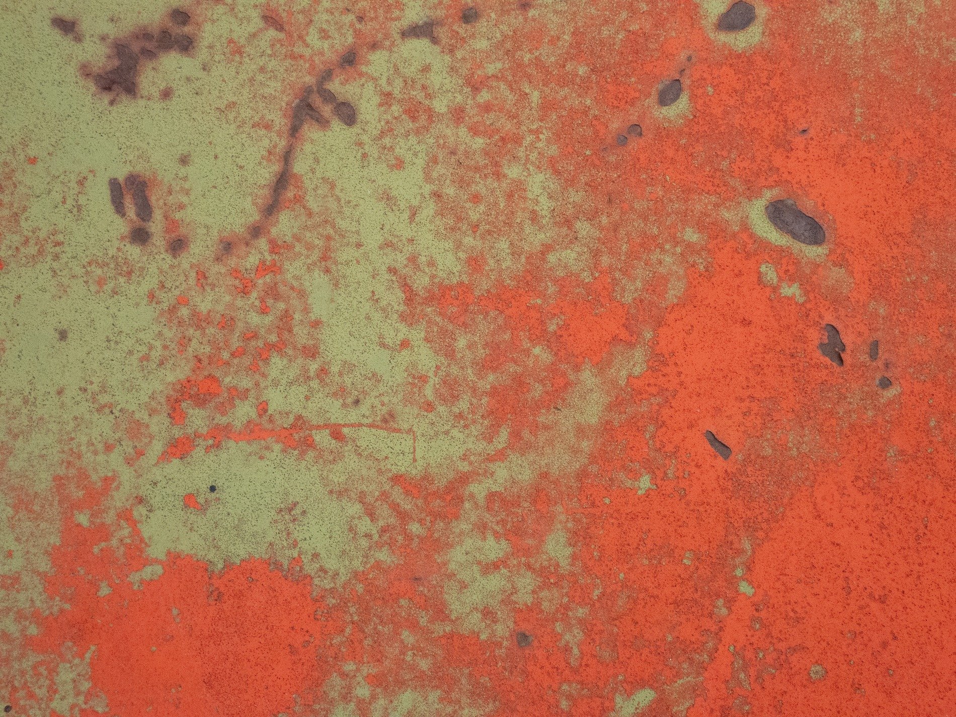 Red paint wears away, pale green surface shows beneath, dark rust claims the soul