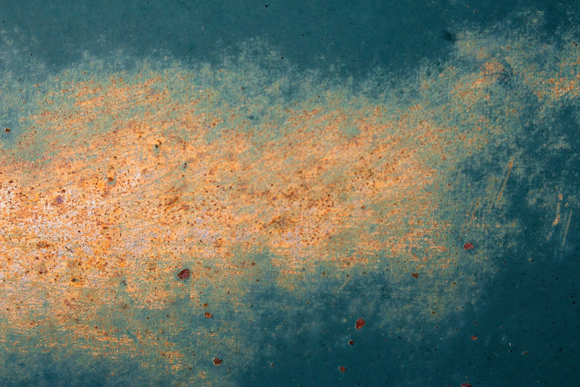 Rust blooms on the teal, orange dust on metal skin, time eats through the paint