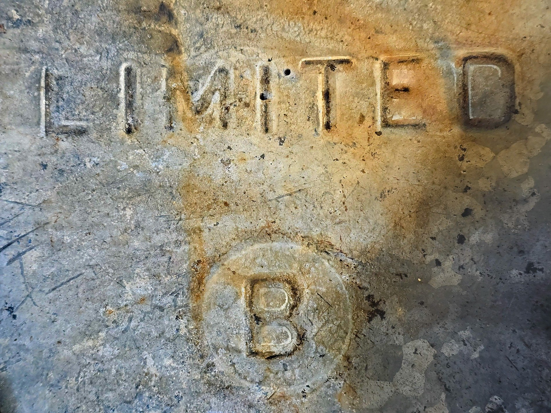 Stamped in cold gray steel, orange rust bleeds through the word, marks of age remain