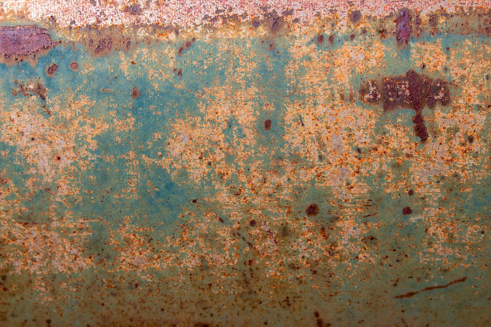 Teal skin flakes away, orange grit claims the surface, years leave a deep trace