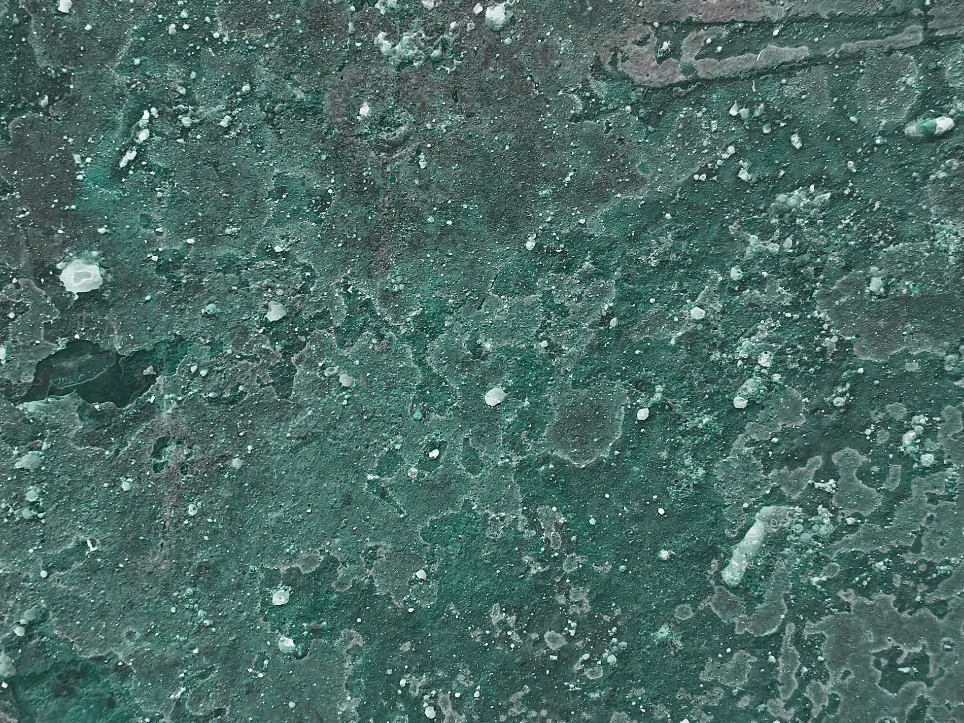 Teal skin peels away, white salt blooms on the surface, layers of decay