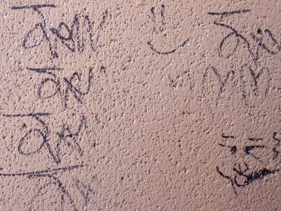 Black ink on the wall, rough stone holds a hidden face, fading marks remain