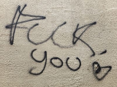 Black paint on the wall, harsh words flow in cursive script, small heart ends the tag