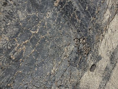 Black road starts to break, spider webs of tiny cracks, sun bleaches the stone