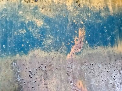 Blue band wears away, pitted metal meets the light, rust blooms in the gaps