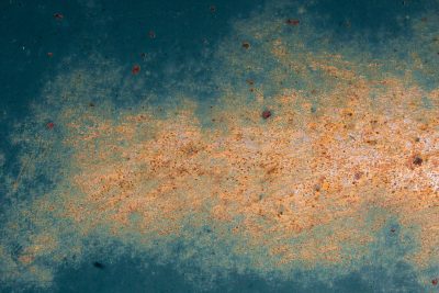 Teal paint wears away, orange oxidation blooms, metal surface scars