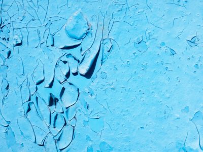 Blue paint curls away, deep cracks map the aged surface, shadows fall on chips