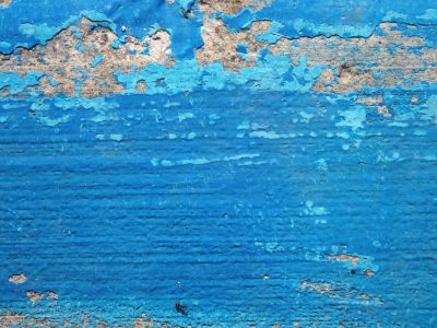 Blue paint flakes away, concrete shows through the gaps, time peels back the skin