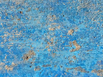 Blue paint flaking thin, stony grit breaks through the skin, weathered ground remains