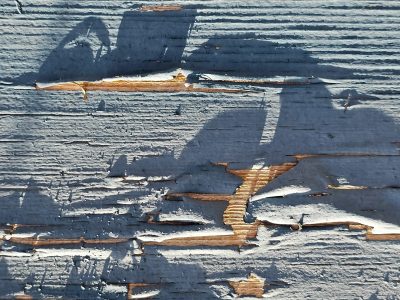 Blue paint peels away, golden wood reveals its grain, shadows stretch across