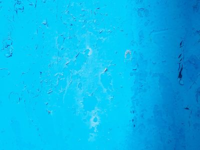 Blue paint starts to curl, fractured surface tells a tale, chips fall to the ground