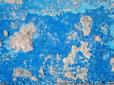 Blue paint starts to peel, rough grey concrete hides beneath, time wears down the skin