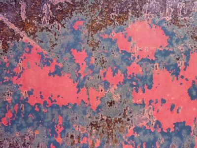 Red flakes peel away, rusted steel breathes through the gaps, time strips the surface