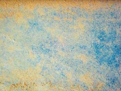 Blue wash fades away, golden sand beneath the sea, weathered stone remains