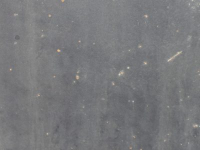 Charcoal metal skin, orange rust blooms like small stars, steel awaits the rain