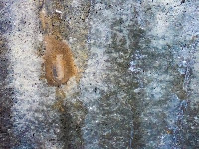 Cold grey surface breaths, amber stain blooms on the stone, shadows dance in dust