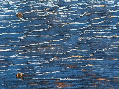 Cracked blue paint retreats, weathered grain shows through the gaps, rusty nails remain