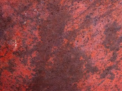 Crimson oxide spreads, pitted metal holds the heat, iron flakes away