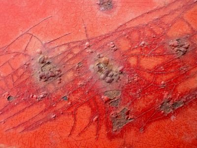 Crimson paint blisters, iron breaks the brittle shell, time cracks the surface