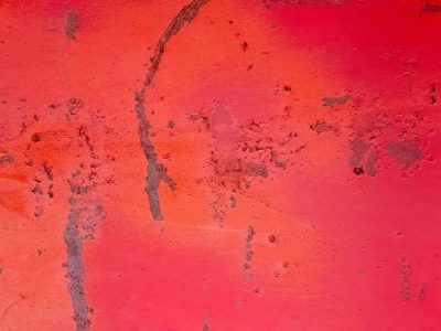 Crimson surface wears, dark stains mark the metal wall, time leaves textured scars