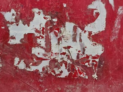 Crimson surface wears, white fragments cling to the red, paper torn by time