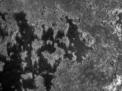 Dark pits mark the light, jagged grit claims the heavy field, paths trace the metal