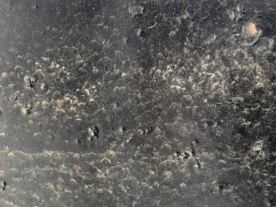 Dark surface is scarred, gritty dust clings to the paint, shadows fill the pits