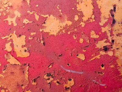 Red flakes fall away, golden patches show beneath, layers crack and peel