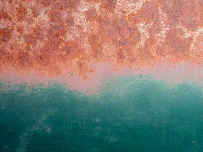 Orange rust creeps down, teal paint holds the line against, time eats through the steel