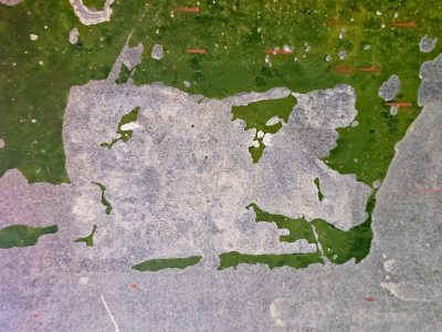 Green paint flakes away, gray stone surface is revealed, layers of decay