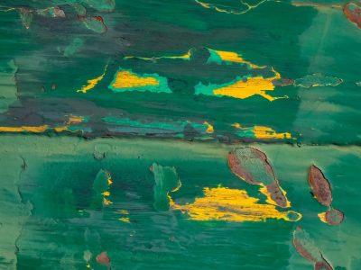 Green paint flakes away, yellow layers meet the rust, time peels back the skin