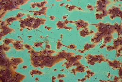 Green skin flakes away, orange pits trace the heavy metal, grit marks the finish