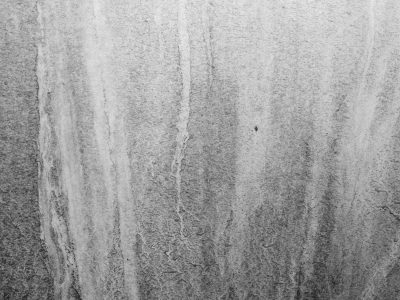 Grey wall meets the rain, dark stains run down textured stone, time leaves silent tracks
