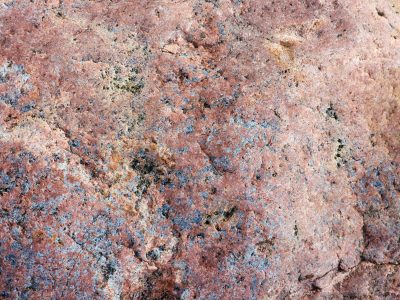 Pink rock wears its age, dark grains fleck the rugged face, time rests in the grain