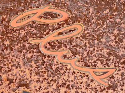 Logo paths meet the rust, heavy grit claims the surface, time marks the metal