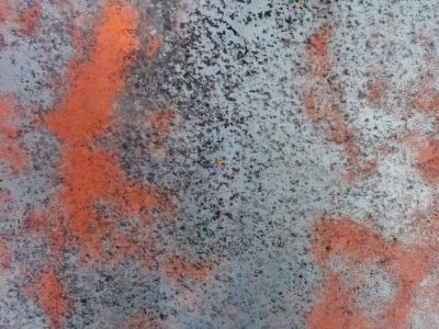 Orange blooms on grey, iron oxide eats the steel, weathered metal skin