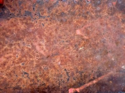 Orange iron flakes, deep brown shadows pool in pits, slow decay of steel