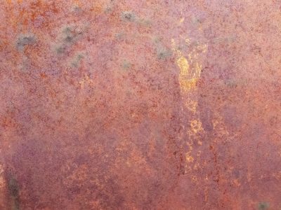 Orange dust takes hold, iron blooms in mottled hues, metal yields to time