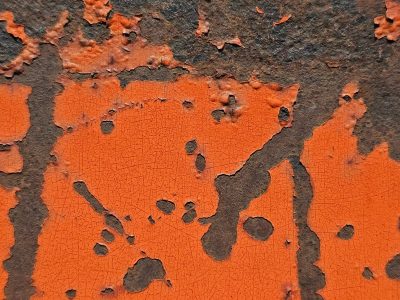 Orange paint peels back, dark rust eats the metal skin, time cracks the surface
