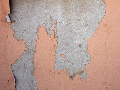 Orange paint peels back, rough wall hides beneath the crust, weather chips away