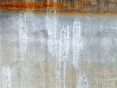 Orange rust bleeds down, silver surface wears away, cold metal endures