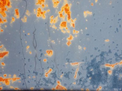 Orange rust breaks through, faded blue paint flakes away, metal starts to turn