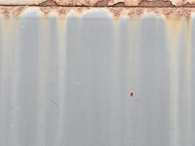 Orange rust creeps down, grey steel wears a weathered coat, time stains the surface